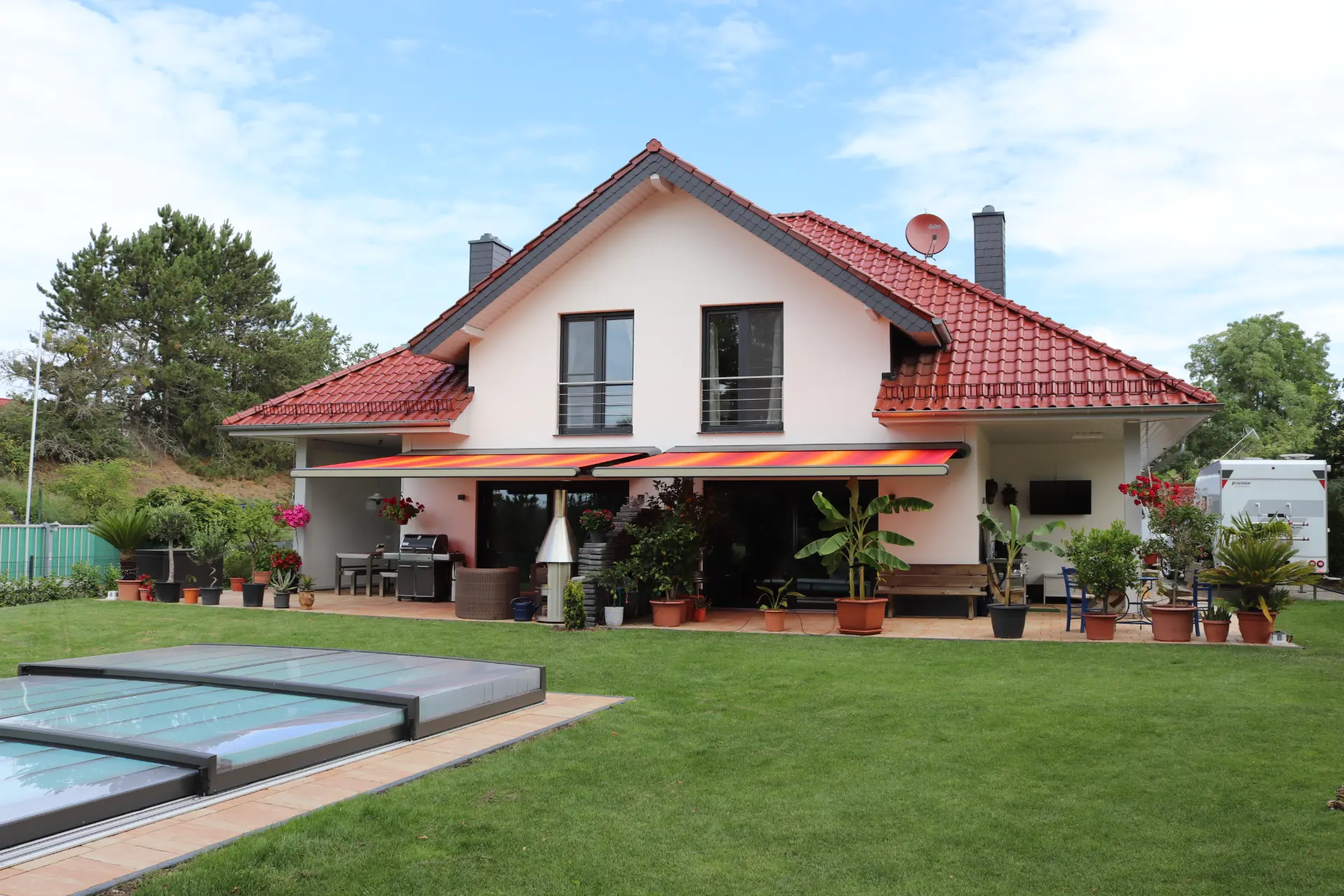 Ausgefahrene Markise mit Sonnenuntergangsmuster über einer Terrasse mit Rattan-Loungemöbeln, im Vordergrund ein abgedeckter Pool
