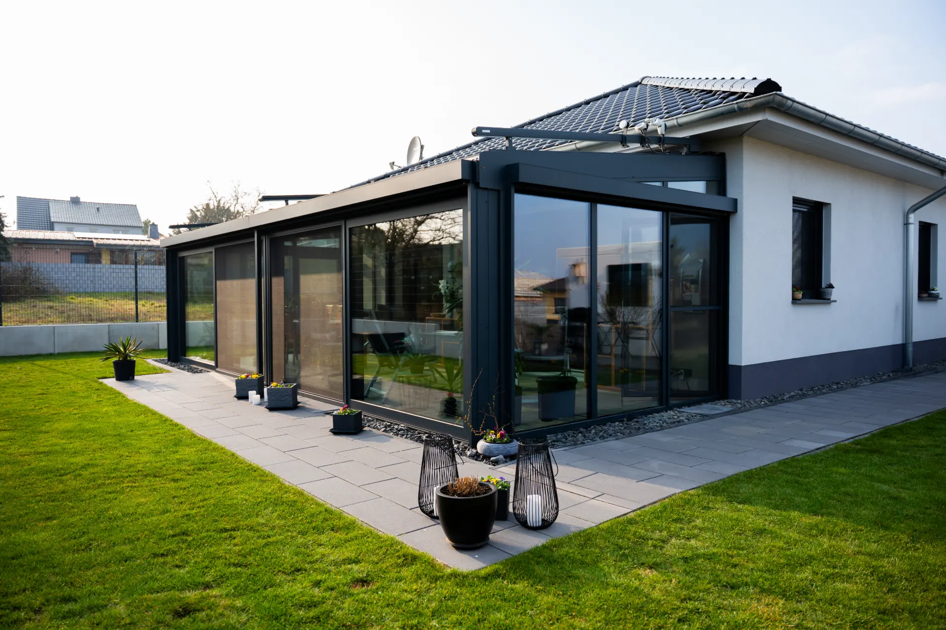 Glasveranda mit großen Schiebeelementen an einer gepflasterten Terrasse mit Windlichtern im Abendlicht