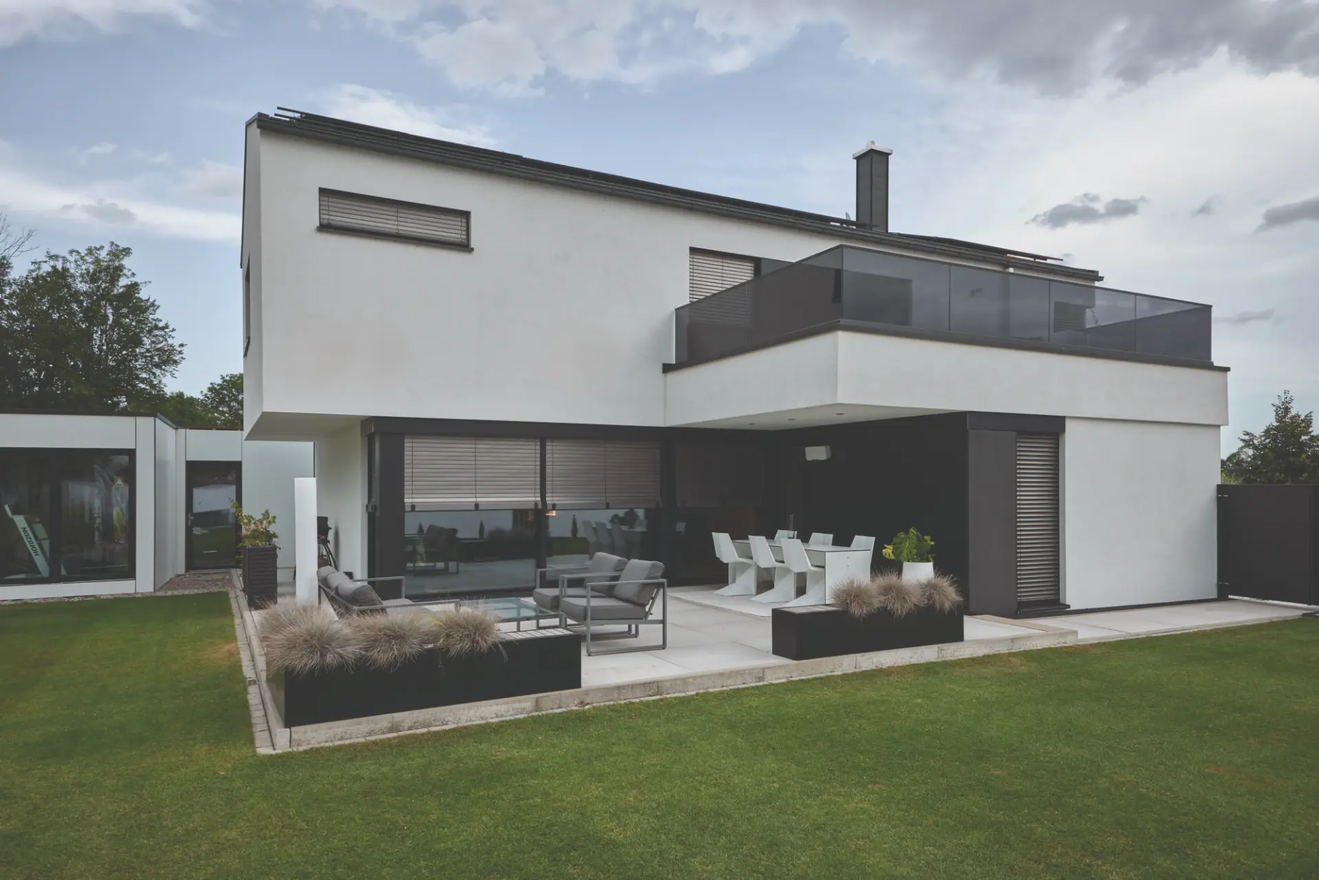Weißes Flachdachhaus mit anthrazitfarbenen Raffstores und Rollladen, davor eine Terrasse mit Loungemöbeln