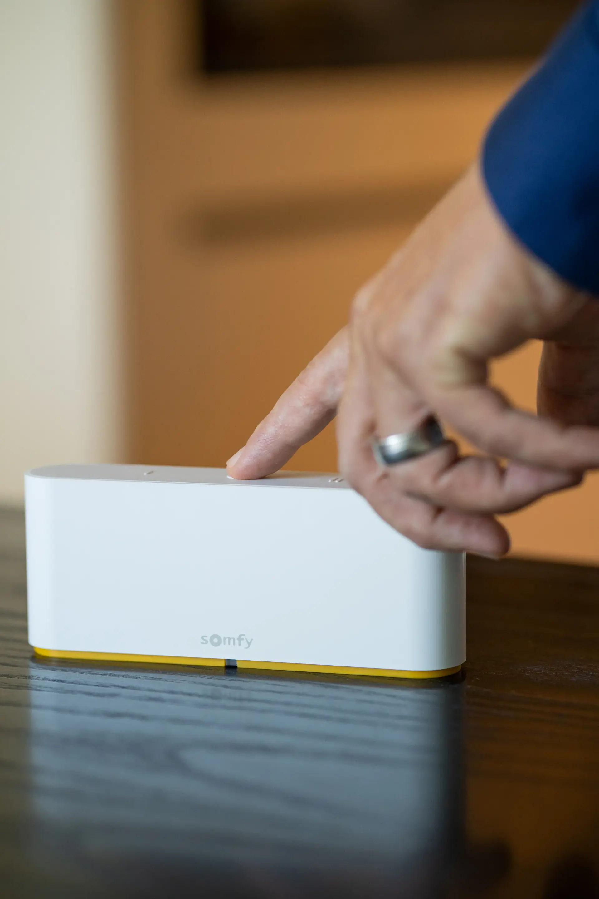 Eine Hand drückt die Taste einer Smart-Home-Steuerzentrale auf einem dunklen Holztisch