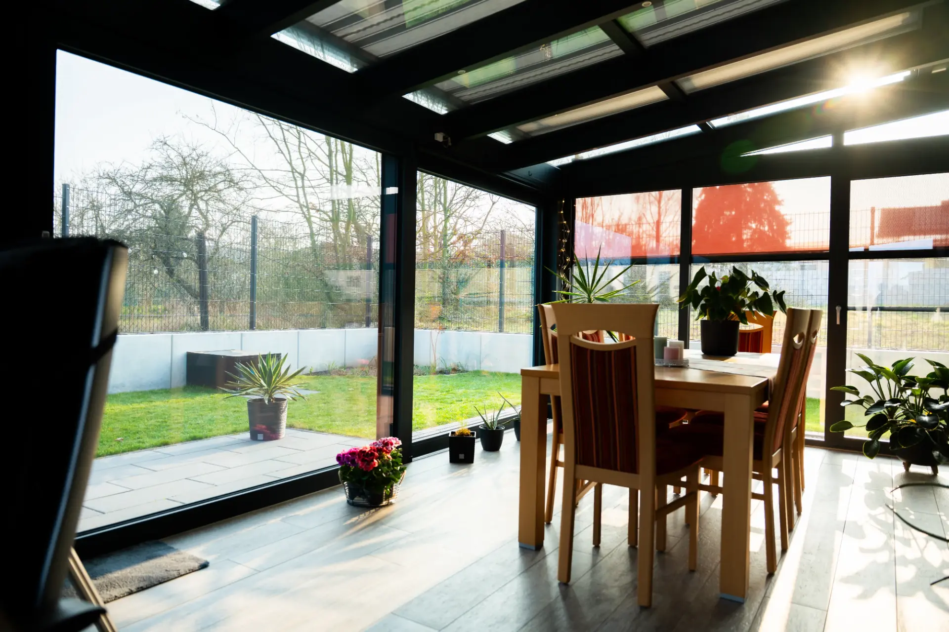 Wintergarten mit Esstisch und Zimmerpflanzen, durch die Glasfront Blick auf den winterlichen Garten